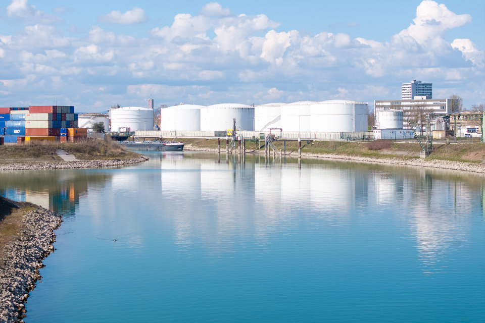 Hafenbecken in Ludwigshafen mit ruhigem Wasser, Containern, großen Tankanlagen und Industriegebäuden am Ufer.